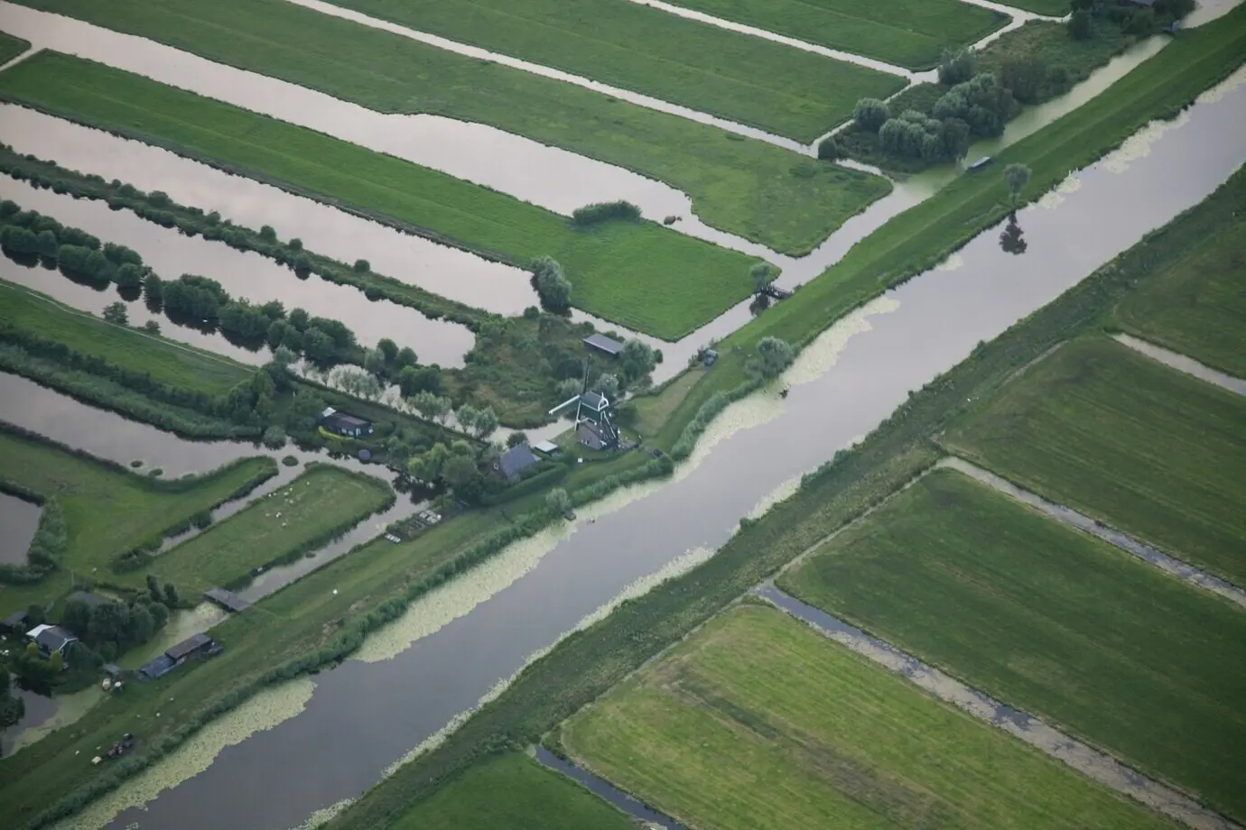 Aufnahme aus erhöhter Perspektive eines Wasserlaufs inmitten eines grasbewachsenen Feldes in einem niederländischen Polder.